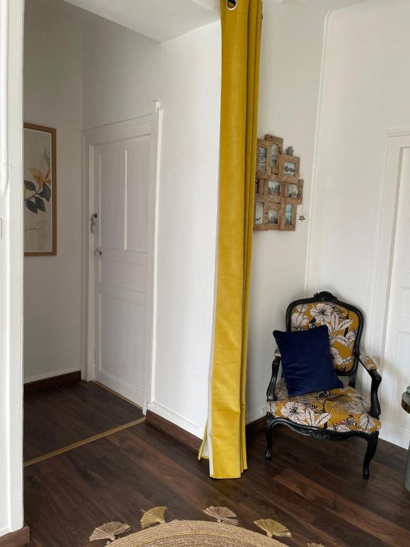 um quarto com uma cadeira e uma cortina amarela em Les Hirondelles de la villa des roses em Pontmain