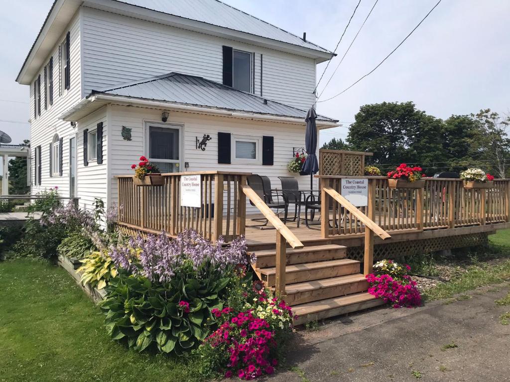 a house with a wooden deck with flowers at The Coastal Country House in New Brunswick in Cape Tormentine