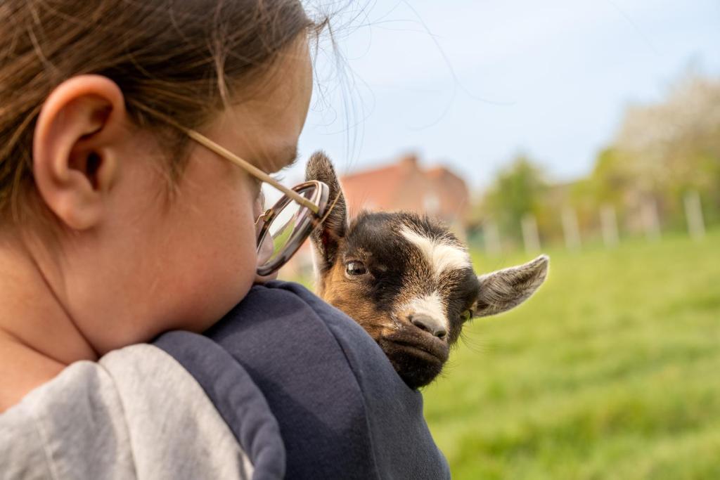 a young girl holding a baby goat in her arms at Logements insolites à la ferme - Yourte, Kota ou Pod in Farbus