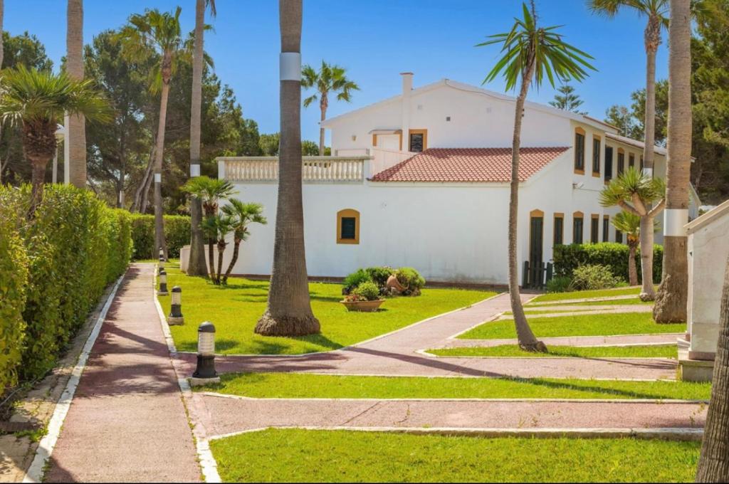 a white house with palm trees and a pathway at Bonito apartamento con terraza, jardín y piscina in Cala en Bosc