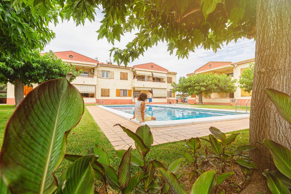 una mujer está sentada junto a una piscina en Apartamentos Aigua Oliva, en Vinarós