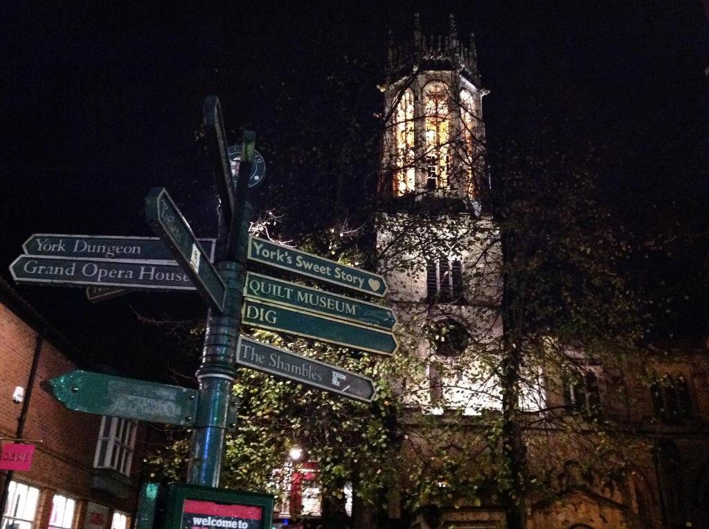 un palo con segnali stradali davanti a una torre dell'orologio di Coppergate Apartments a York