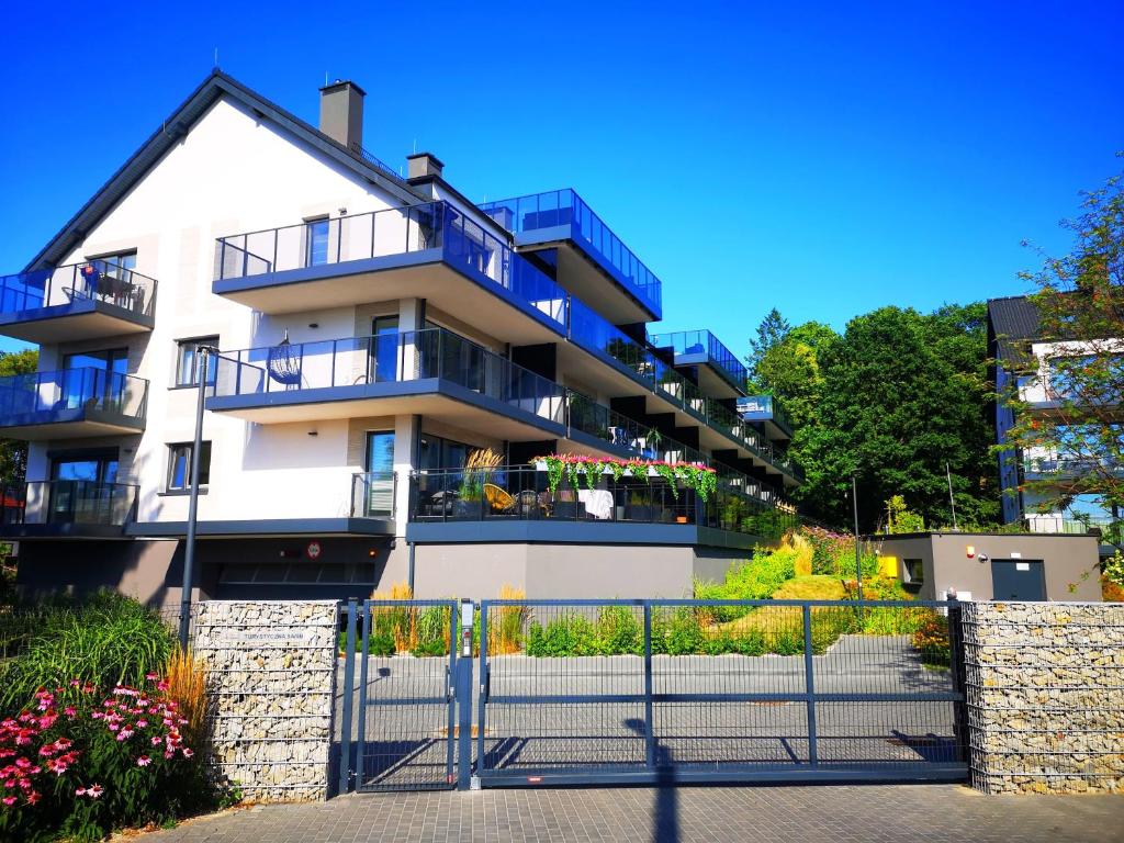 ein weißes Apartmenthaus mit Balkonen und einem Zaun in der Unterkunft Apartament Twierdza z widokiem na jezioro in Ostróda