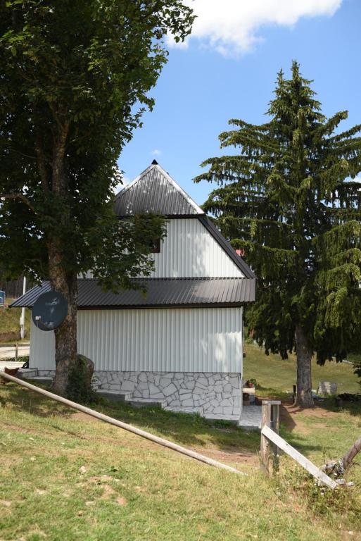 a white building with a tree next to a field at VUKOVIC HOUSE-MOTICKI GAJ in Žabljak