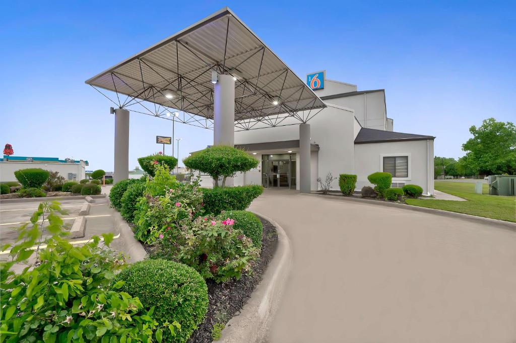 un grand bâtiment blanc avec des plantes devant lui dans l'établissement Motel 6-Denison, TX, à Denison