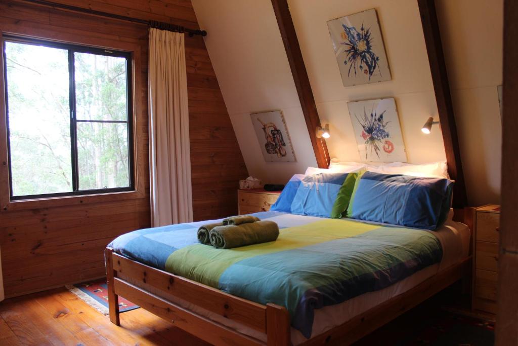 1 dormitorio con cama con sábanas azules y ventana en Green Leaves Cabin, en Denmark