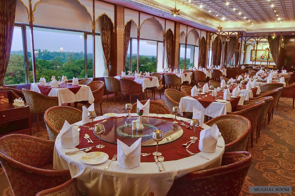 a dining room with tables and chairs and windows at Hotel Clarks Shiraz in Agra