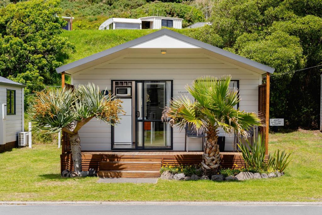 una pequeña casa con palmeras delante en Bowentown Beach Holiday Park, en Waihi Beach