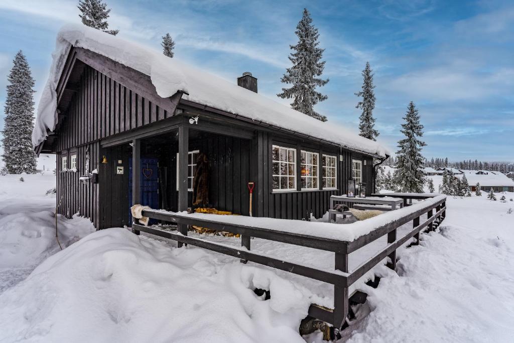 een zwart gebouw bedekt met sneeuw met een hek bij Cottage right next to cross country tracks in Ringsaker