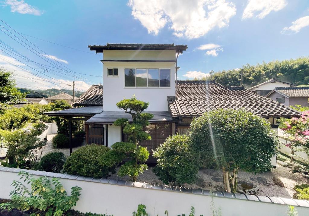 een wit huis met een hek en bomen bij Akizuki Gallery House in Asakura