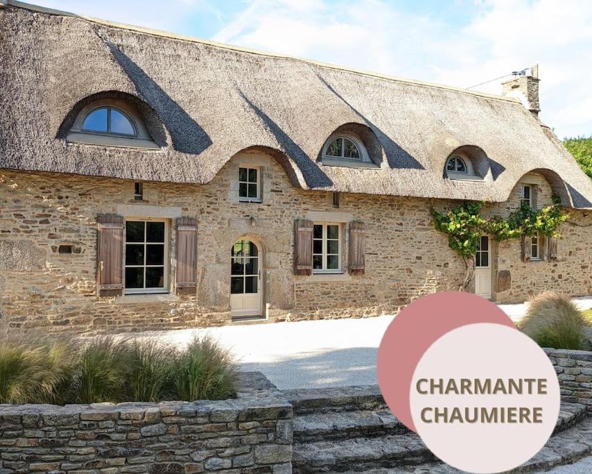 a stone house with a sign in front of it at Maison typique bretonne avec toit de chaume in Camors