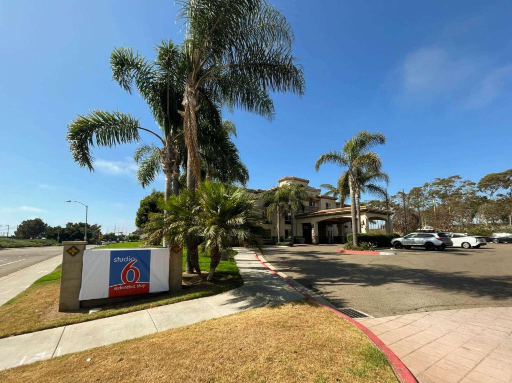 a sign in front of a house with palm trees at Studio 6 Carlsbad CA in Carlsbad