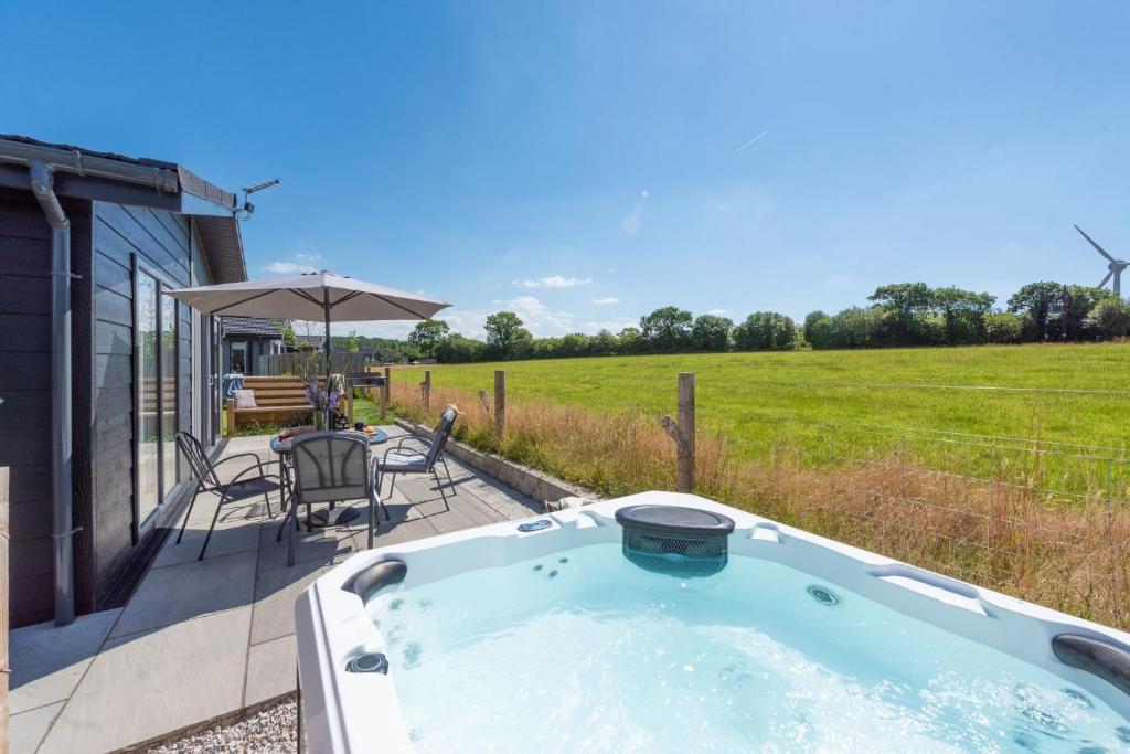 einen Whirlpool auf einer Terrasse mit einem Tisch und Stühlen in der Unterkunft Periwinkle Lodge, 3 Roadford Lake Lodges in Lifton