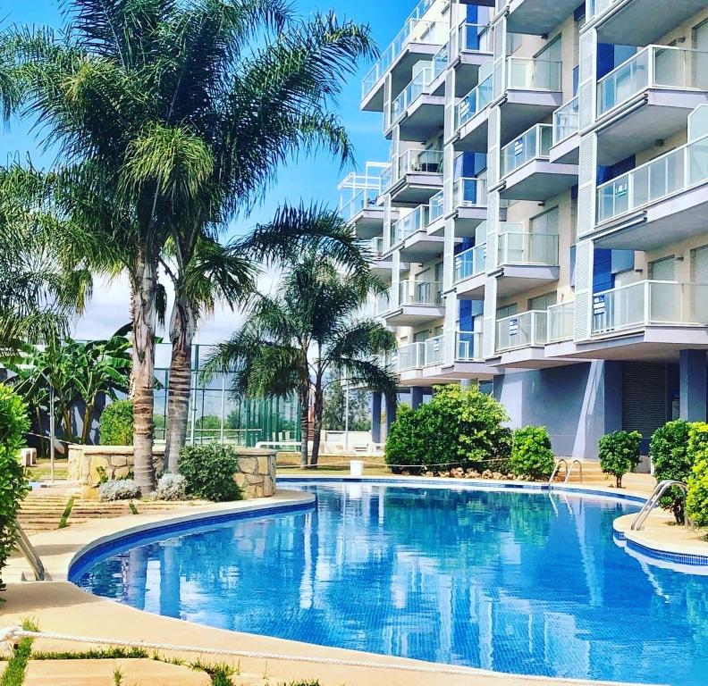 a swimming pool in front of a building with palm trees at The Apartment Olivia in Moncófar