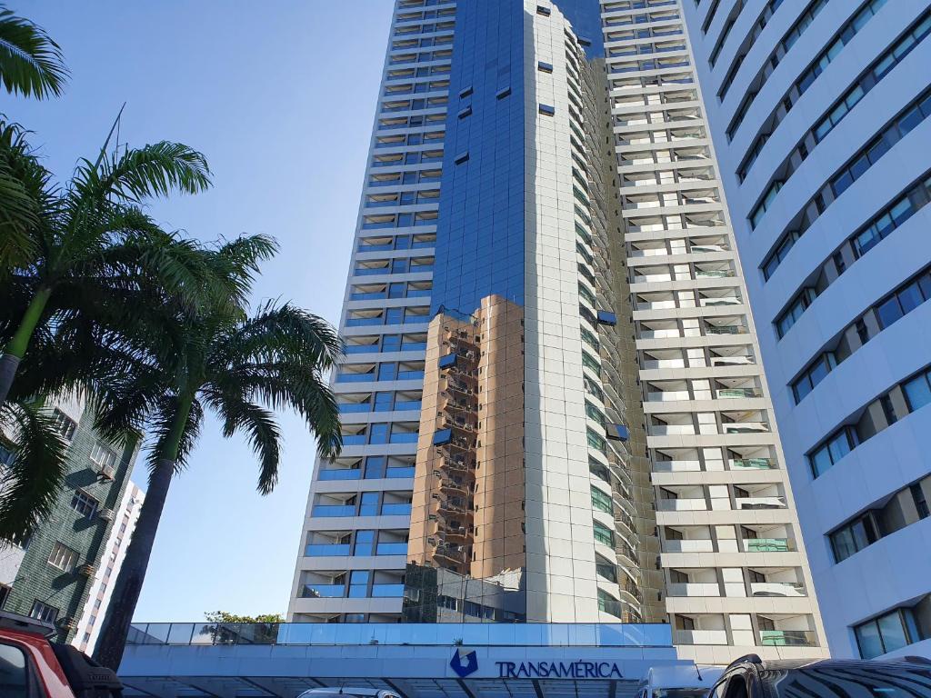un edificio alto con una palmera delante de él en Flat Beach Class Internacional, en Recife