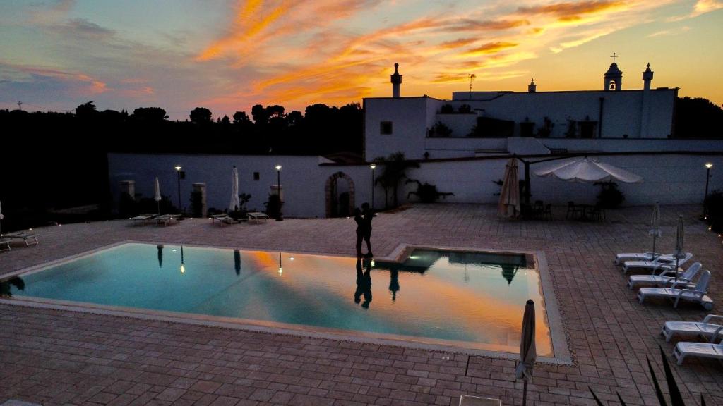 una persona de pie junto a una piscina al atardecer en Masseria Del Crocifisso, en Polignano a Mare