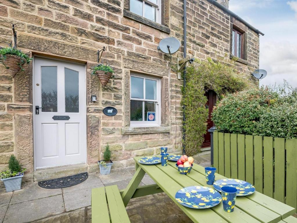 a green picnic table in front of a brick house at Peak Cottage in Bakewell
