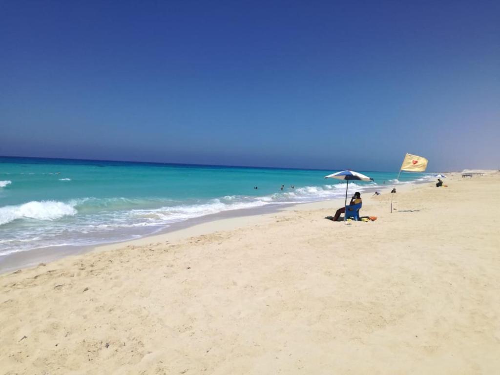 una persona sentada bajo una sombrilla en la playa en Villa Yasmin404, en Marsa Matruh