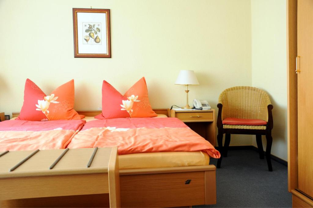 ein Schlafzimmer mit einem Bett mit orangefarbenen Kissen und einem Stuhl in der Unterkunft pension Helga in Bad Dürkheim