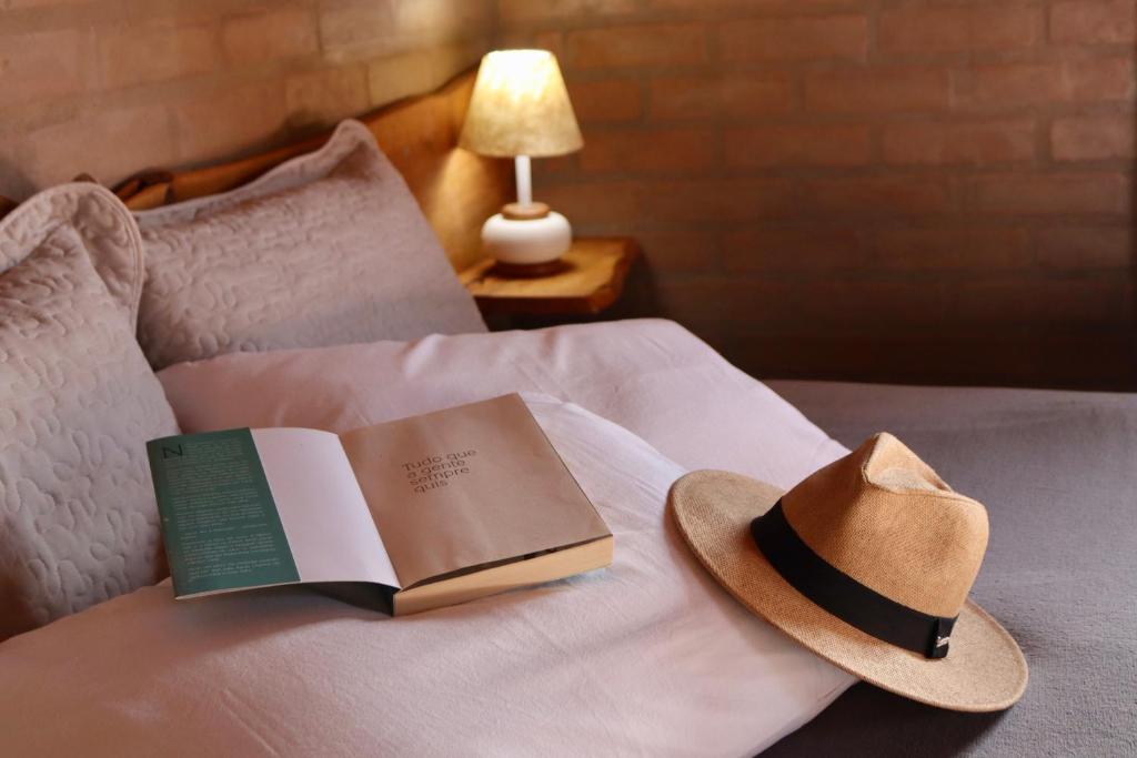einen Hut und ein Buch auf dem Bett in der Unterkunft Refúgio Horse in Santo Antônio do Pinhal