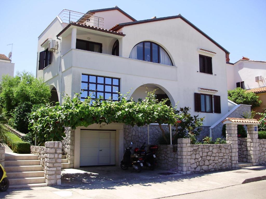 a white house with a motorcycle parked in front of it at Apartments with a parking space Mali Losinj (Losinj) - 8024 in Mali Lošinj
