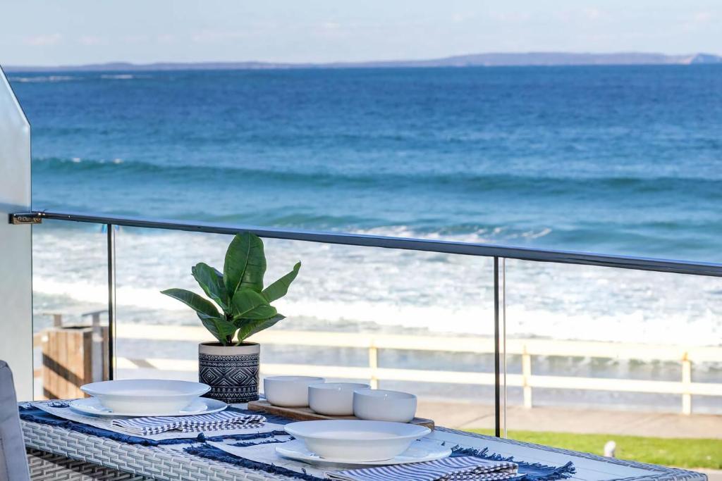 a table with plates and bowls on a balcony with the beach at Mariners 6 in Mollymook