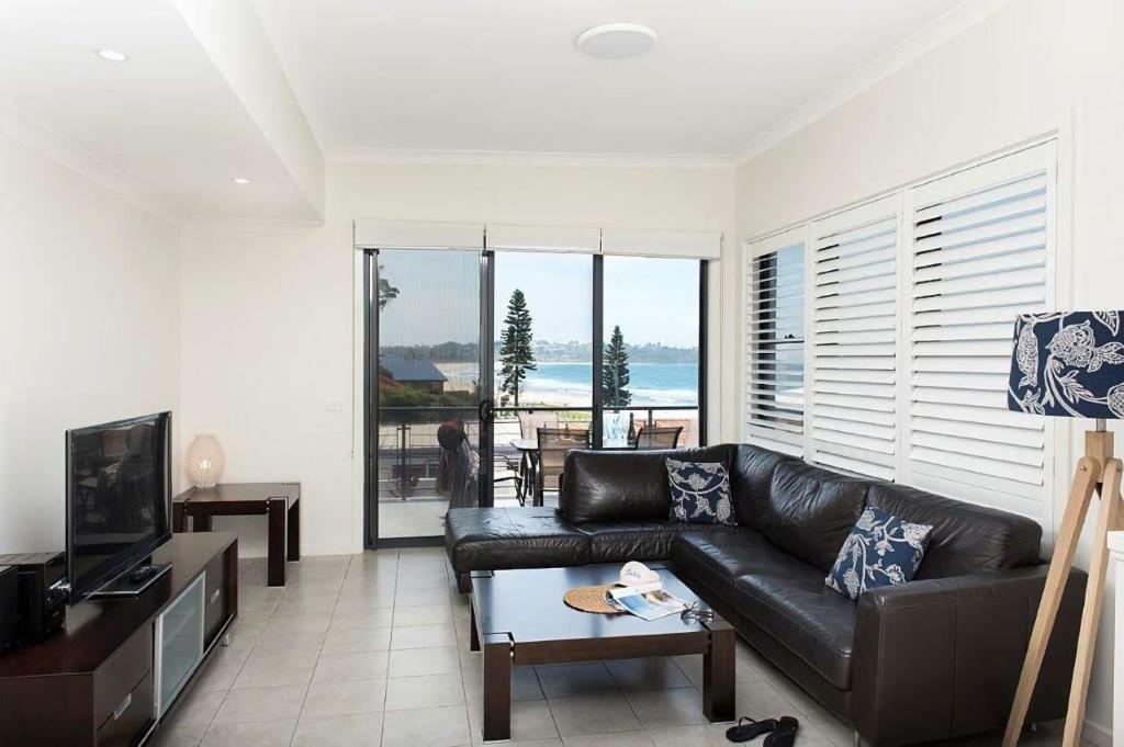 a living room with a black leather couch and a television at Beachfront Eight in Mollymook