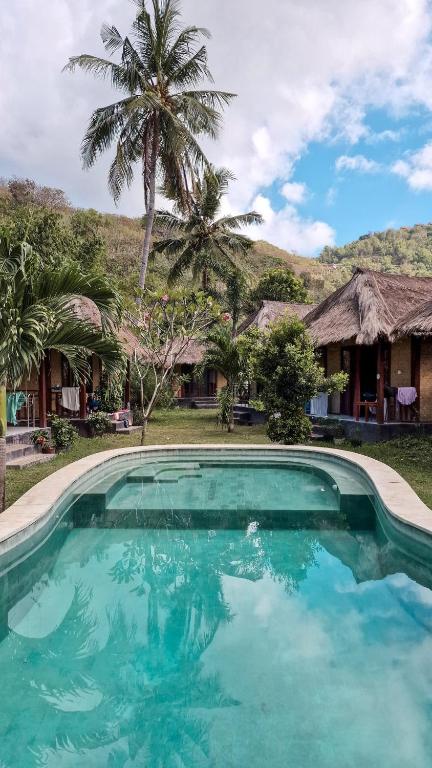 a swimming pool in front of a house with palm trees at Airas' Garden Homestay ECO Bungalows in Kuta Lombok
