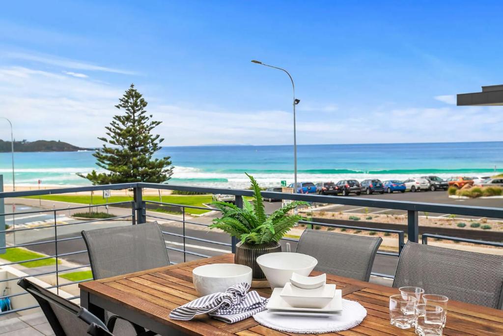 a table on a balcony with a view of the beach at Beachfront Six in Mollymook