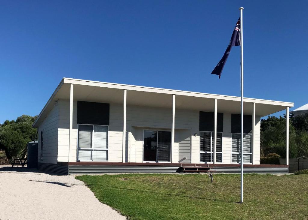 a white house with a flag pole in front of it at Kangaroo Pause Holiday home at Clayton Bay in Clayton Bay