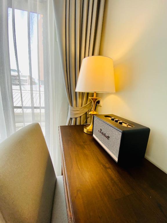 A narrow wood desk beside a curtained window, with a lamp and Marshall speaker.
