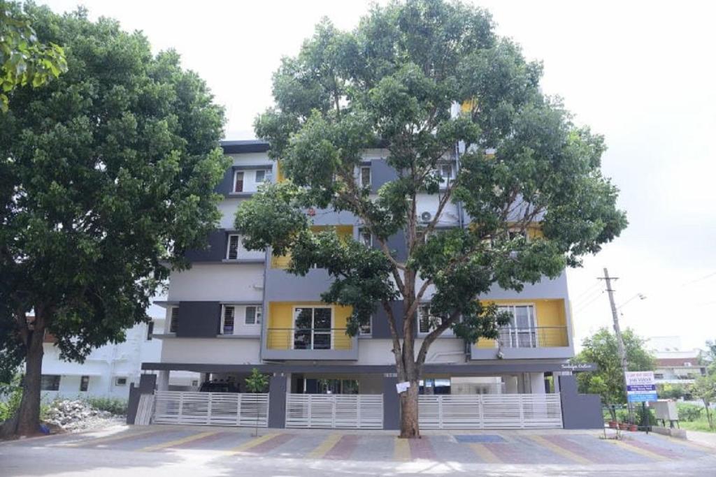 un edificio con un árbol delante de él en The Vihar service Apartment en Mysore