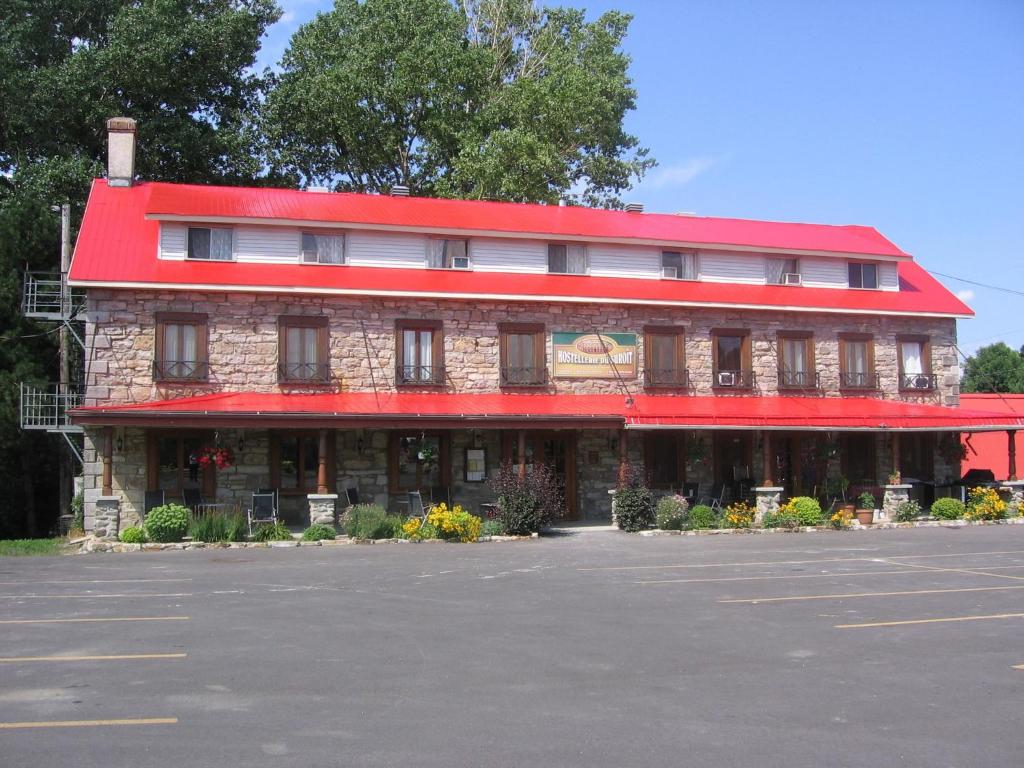 a red building with a red roof on a parking lot at Hostellerie du Suroît in Beauharnois