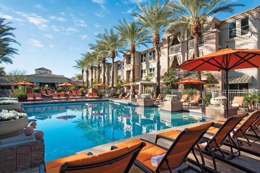 einen Pool in einem Hotel mit Stühlen und Sonnenschirmen in der Unterkunft Sonesta Suites Scottsdale Gainey Ranch in Scottsdale