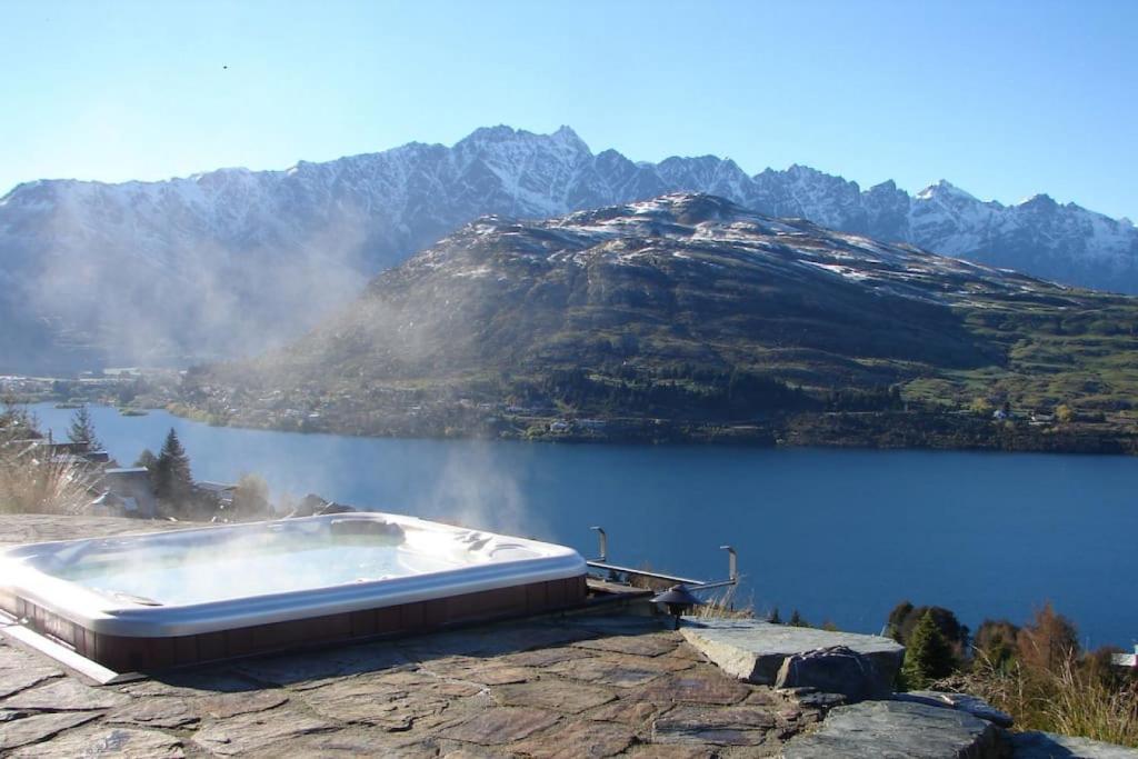 a bath tub sitting on a rock next to a lake at Goldleaf Hill -Spa Pool -Lake Views- 4 Bedrooms in Queenstown