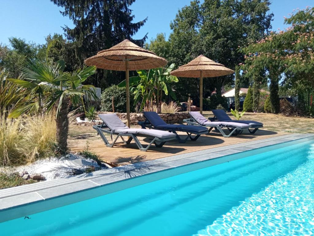 a group of chairs and umbrellas next to a swimming pool at Mas des Vignes Piscine chauffée in Le Champ-Saint-Père