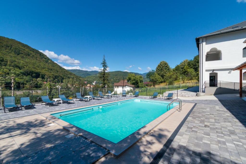 a swimming pool with chairs and a house at Casa Basarab in Călimăneşti