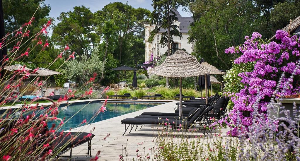 馬爾塞揚的住宿－Domaine Tarbouriech, Hôtel & Spa，游泳池配有椅子、遮阳伞和紫色鲜花