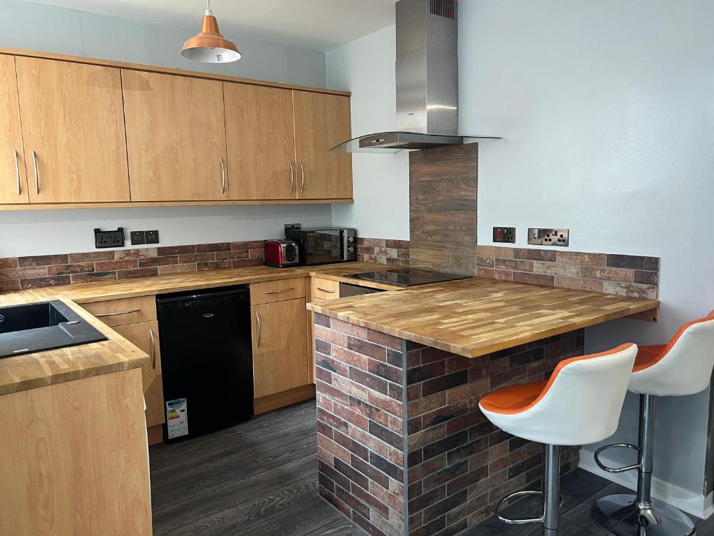 una cocina con armarios de madera y una barra con taburetes en The Black Isle Retreat en Inverness