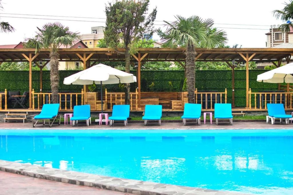 a swimming pool with blue chairs and umbrellas at Hotel Genatsvale in Batumi