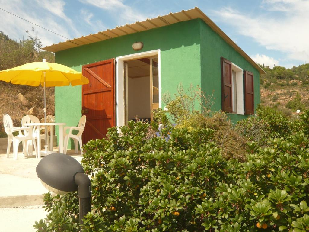 una piccola casa verde con tavolo e ombrellone di Verde a Santa Margherita di Pula
