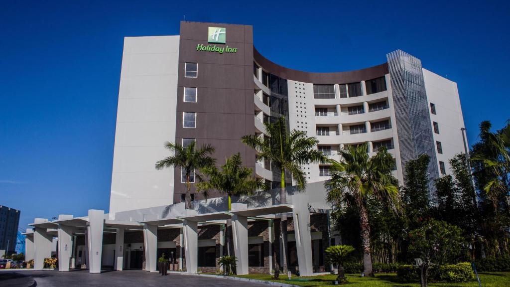 Holiday Inn Tuxpan - Convention Center, an IHG Hotel في توكسبان دي رودريغيز كانو: عماره فندقيه امامها نخيل