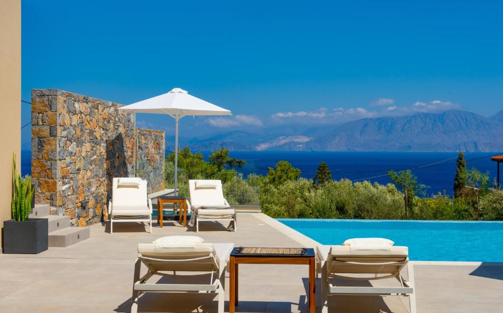 uma piscina com cadeiras, uma mesa e um guarda-sol em Mirabella Hills em Agios Nikolaos