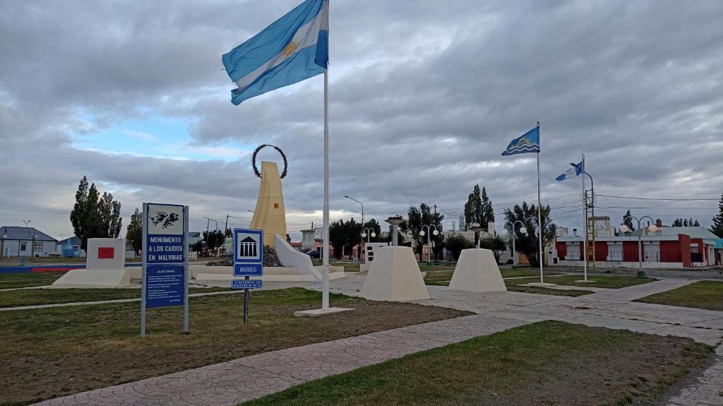 Un monumento con dos banderas en un parque con señales en 100 años ciprés, en Río Gallegos