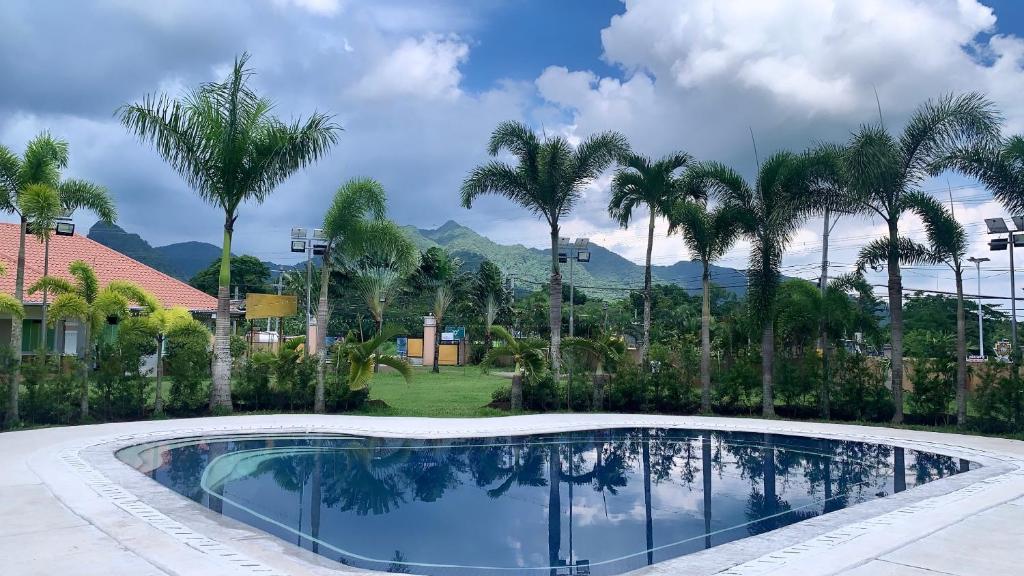 a swimming pool with palm trees and mountains in the background at 3 Peaks Resort & Boutique Hotel in Lipa