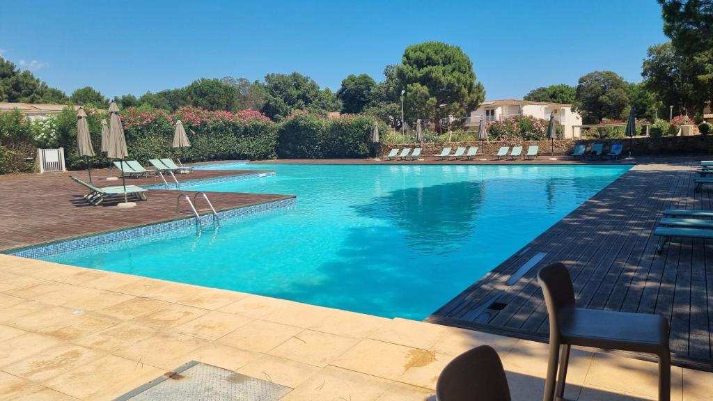 een groot zwembad met stoelen en parasols bij Fiori Di Cala Rossa Très beau studio, 2 adultes 1 enfant moins de 3 ans, au sein d'une résidence hôtelière avec piscine et plage Cala Rossa à 600m in Lecci