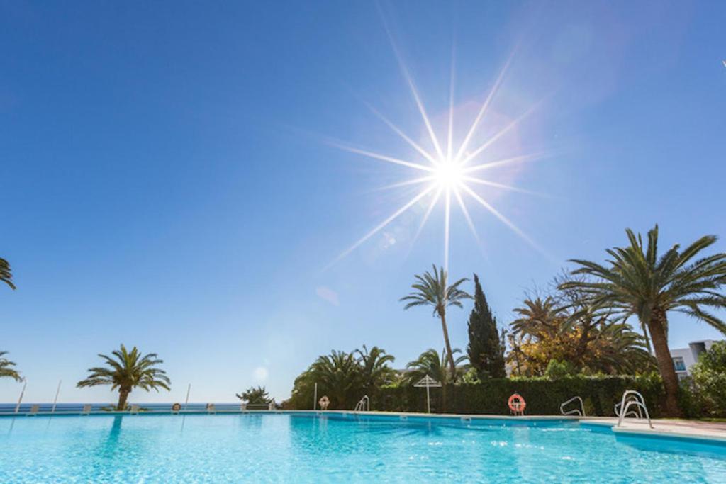 uma piscina com palmeiras e o sol no céu em La Roca Chica em Torremolinos