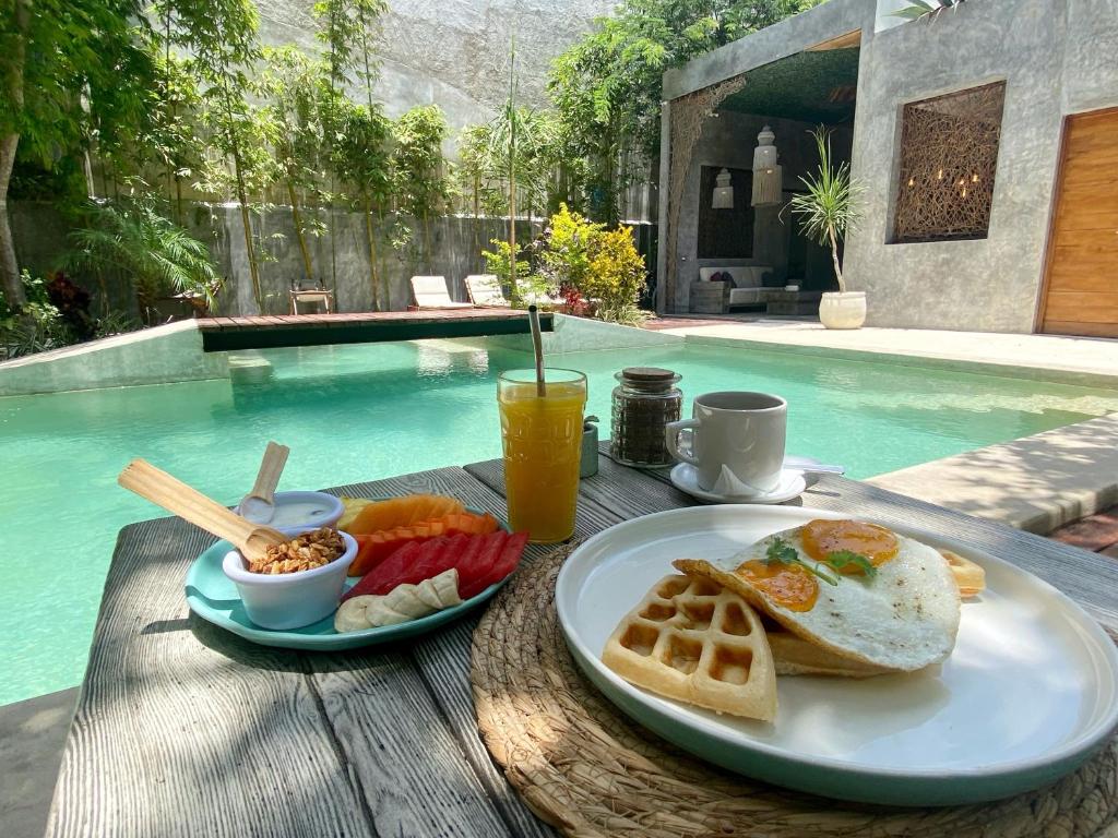 un desayuno con huevos, pan y fruta en una mesa junto a la piscina en Little Gem Hotel Tulum La Veleta en Tulum