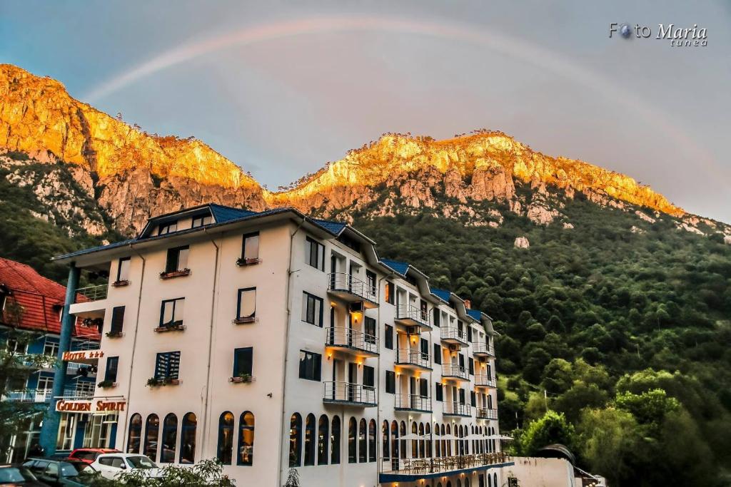 um edifício em frente a uma montanha com um arco-íris em Hotel Golden Spirit em Băile Herculane