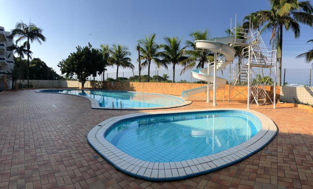 a large swimming pool with a slide and palm trees at Apartamento beira mar - Praia de Boraceia in Bertioga